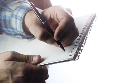 A person writing on a pad of paper with a pen